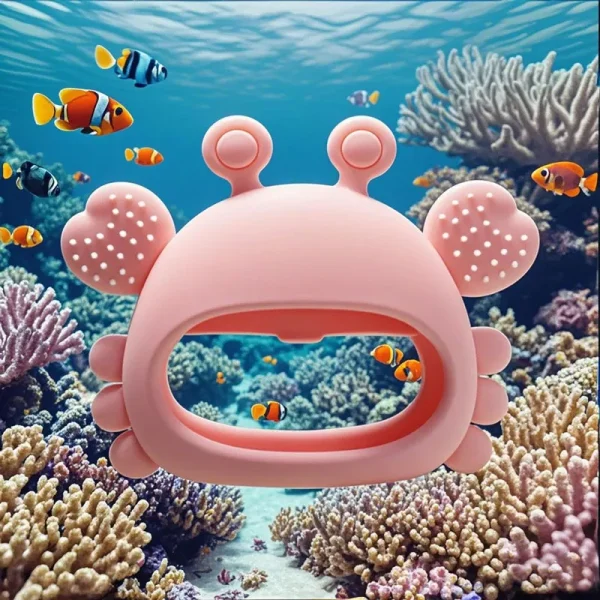 Crab-shaped pink silicone teether toy floating underwater with coral and clownfish background