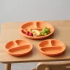 Orange silicone divided suction plates with fruits on a wooden highchair table