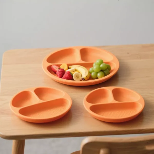 Orange silicone divided suction plates with fruits on a wooden highchair table