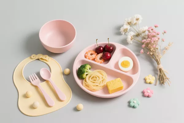 Cream yellow and blush pink silicone baby feeding set with bib, suction plate, bowl, utensils and floral background