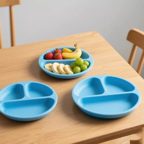 Blue silicone divided baby plates with suction base on a wooden table, filled with fruit