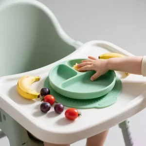 Baby using green silicone suction plate with dividers on highchair tray
