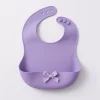 Purple silicone baby bib with built-in food catcher and bow decoration