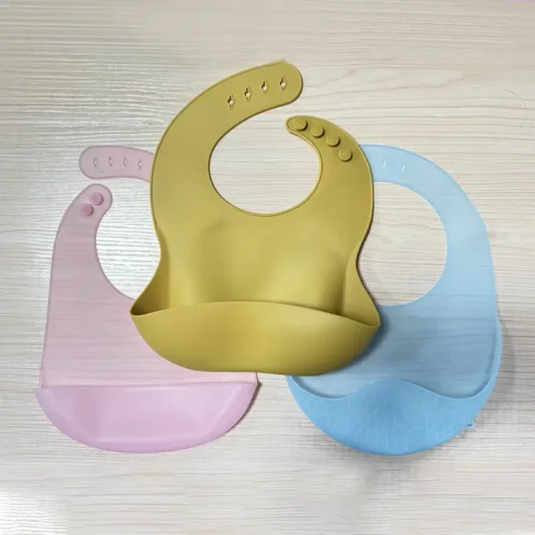 Pink silicone baby bib with adjustable buttons and wide pocket.