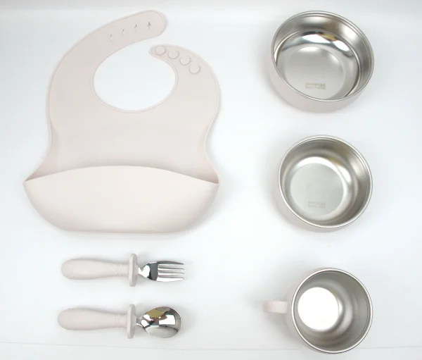 Beige Silicone Baby Meal Kit Beige silicone baby feeding set with bib, bowls, cup, spoon, and fork.